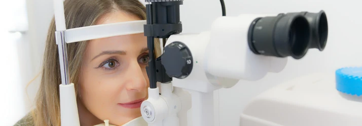 A patient sitting forward with her chin resting on the base of exam machinery during an exam