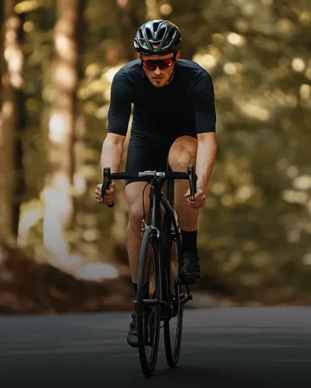 A biker dressed in athletic wear and biking through the woods wearing protective sunglasses
